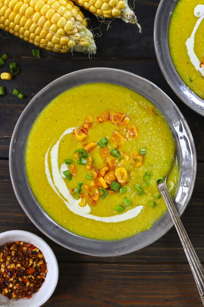 aerial shot of creamy corn soup in a grey ceramic bowl with garnish of cream, green onion, and roasted corn