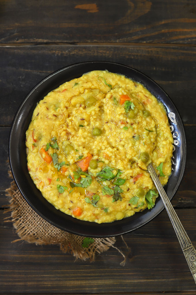aerial shot of daliya khichdi in a black serving bowl with a serving spoon