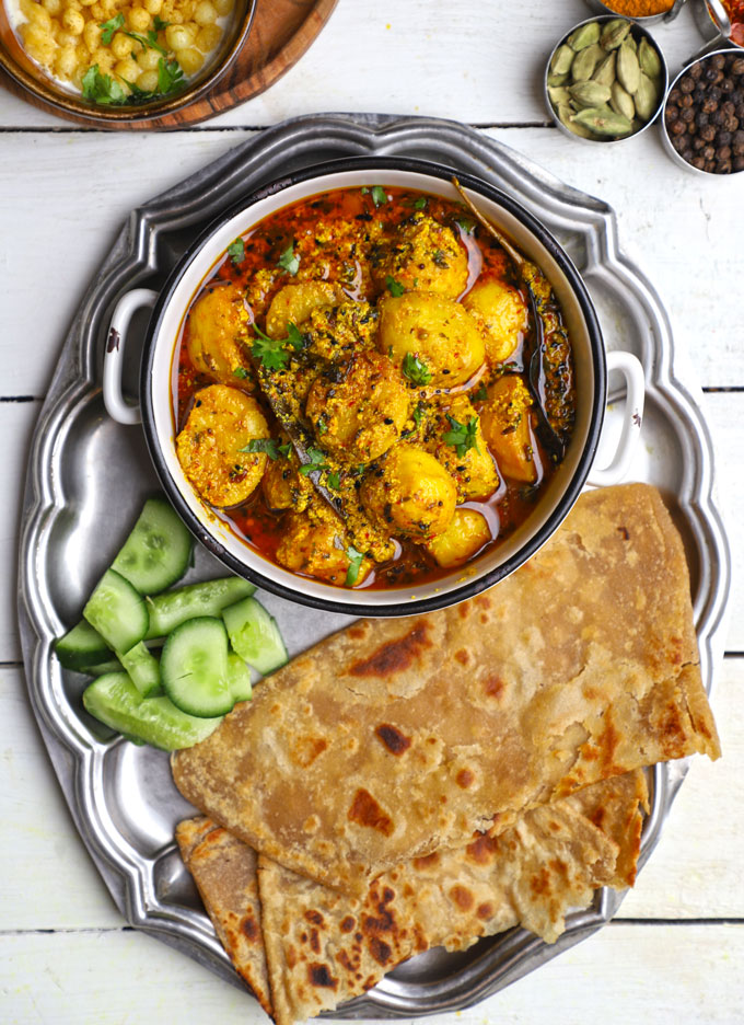 aerial shot of dahi wale aloo in a thali with paratha on a white surface